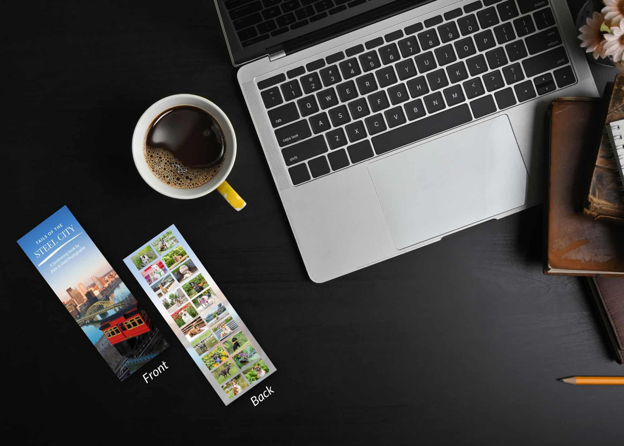 Tails of the Steel City bookmark on a black desk with a computer and cup of coffee